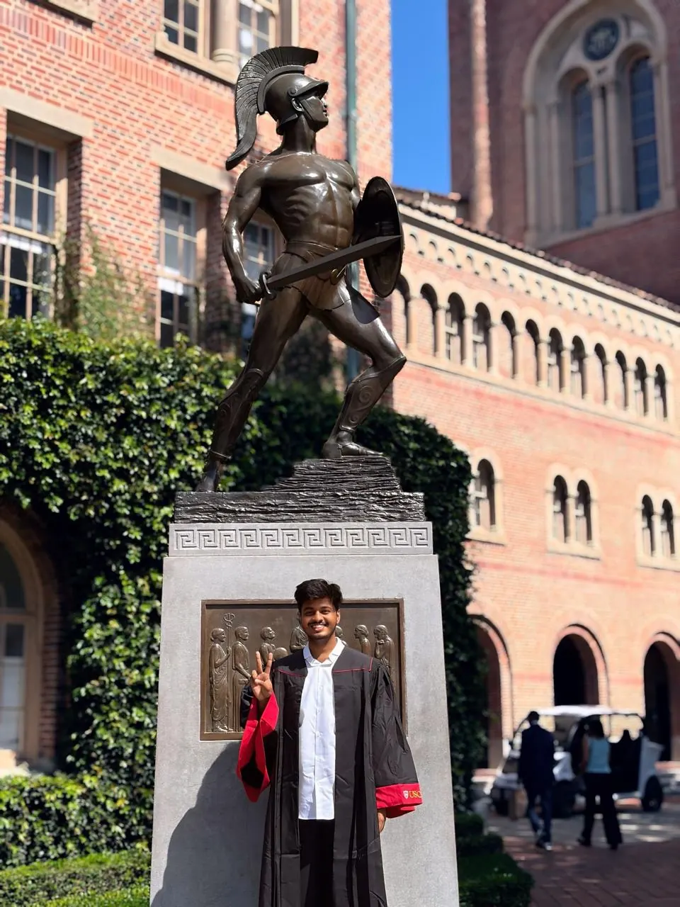 Tarun at his USC graduation, next to the Tommy Trojan statue
